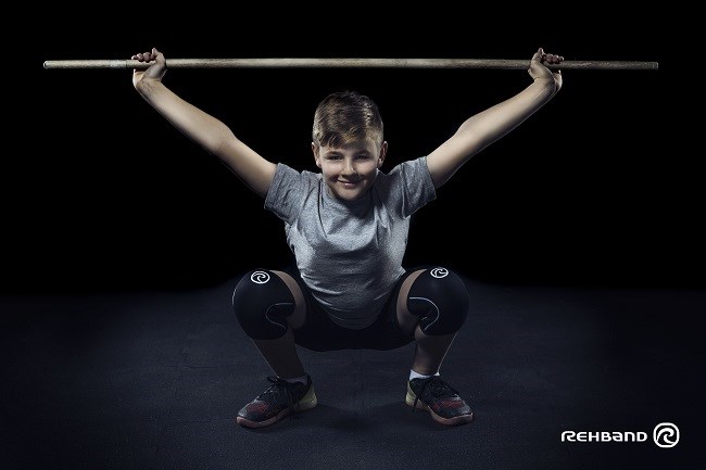 Dreng udfører en overhead squat med vægtstang og Rehbands knæbeskytter.