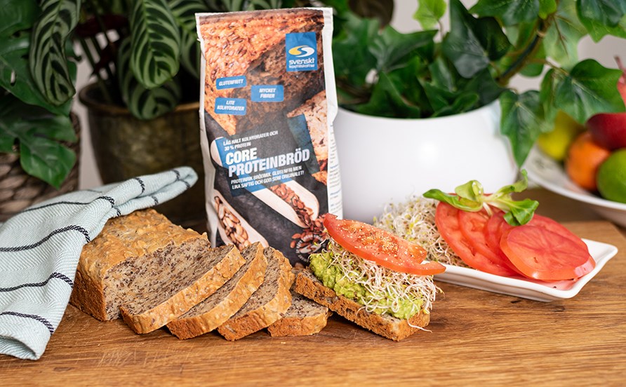 Proteinbrd skret og serveret p en trplade. En skive er pyntet med tomat, acocado og spirer.